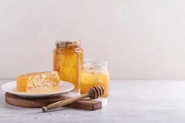 a bottle of chunk honey with a piece of honeycomb on a plate and a jar of raw behind a dipper